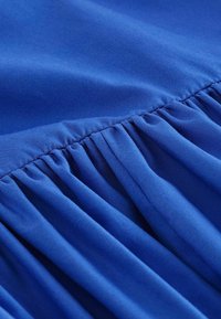 Royal blue fabric with a smooth texture, featuring gathered pleats along the seam, creating a flowing design.