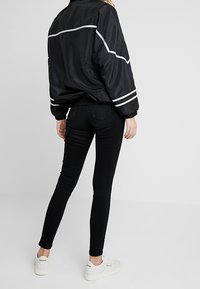 Chaqueta bomber negra con rayas blancas, jeans ajustados negros y zapatillas blancas. Textura suave, ajuste casual y silueta relajada.