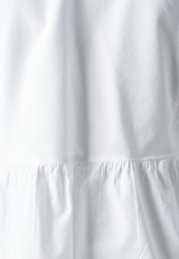 Indumento in cotone bianco con ruffle arricciato sul fondo, caratterizzato da una texture liscia e un design semplice.