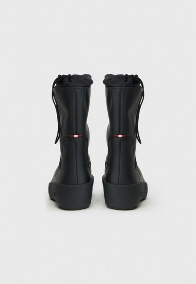 O pereche de bocanci negri până la glezne, cu manșete ajustabile cu șnur, talpă groasă texturată și detalii cu dungi roșii și albe pe spate.