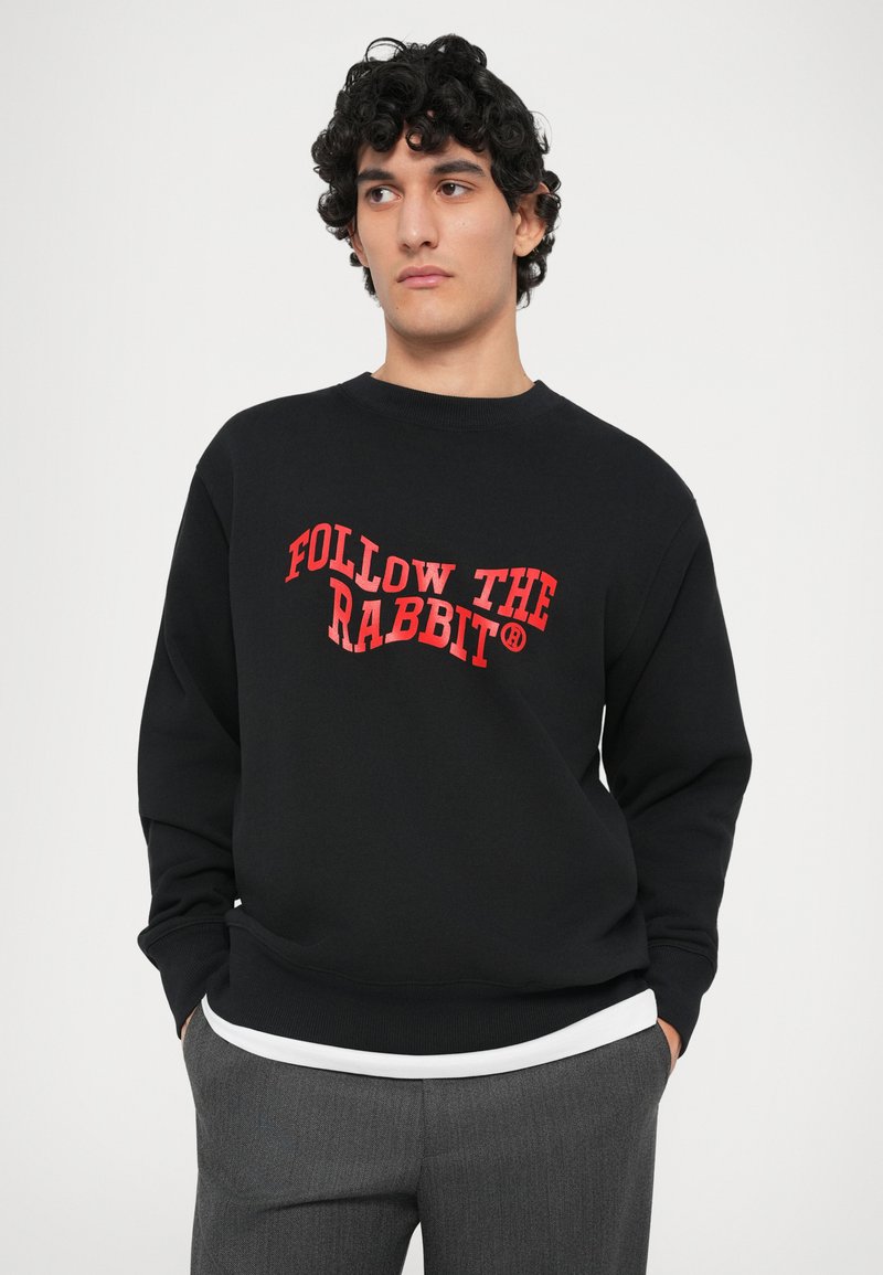 Zwarte sweatshirt met ronde hals, voorzien van in het oog springende rode tekst "FOLLOW THE RABBIT". Zachte stof, lange mouwen en een relaxte pasvorm.