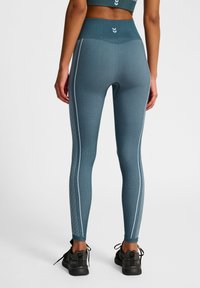 Niebiesko-zielone legginsy z wysokim stanem, teksturowany materiał i białe paski po bokach. W połączeniu z czarnymi butami sportowymi.