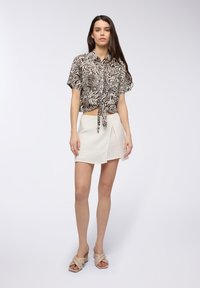 Cropped shirt a stampa zebra in bianco e nero con dettaglio nodo, abbinato a una gonna avvolgente color beige chiaro e sandali con tacco neutri.