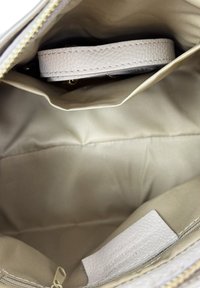 Beżowa torba wnętrze z materiałową podszewką, kieszenią na zamek i złożonym jasnym skórzanym paskiem w środku.