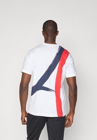 Hvid bomulds t-shirt med et stort navy- og rødt abstrakt design på ryggen. Korte ærmer, klassisk crew neck og afslappet pasform.