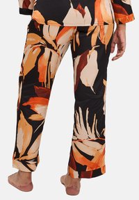 Pantalons de pyjama noirs avec de grands motifs abstraits de feuilles orange et crème. Ils présentent une coupe décontractée et un tissu léger avec une texture lisse.