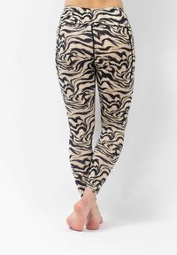 Leggings gemaakt van rekbare stof hebben een beige en zwart golvend patroon, een hoge tailleband en een aansluitend ontwerp.