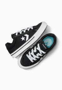 Schwarze Leinensneaker mit weißen Schnürsenkeln, einem weißen Sternlogo und einer kontrastierenden schwarzen Gummizunge. Einzigartiges Design der türkisfarbenen Innensohle.