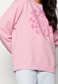 Ljusrosa sweatshirt med rund halsringning, lös passform och långa ärmar som har en geometrisk blomgrafik i mörkare rosa.