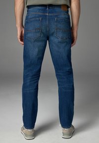 Donkerblauwe denim jeans met een slim fit, voorzien van een leren tailleband patch, twee achterzakken en minimale slijtage.