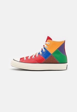 Zapatilla de caña alta con cordones blancos, con un diseño de patchwork en rojo, naranja, azul, verde, morado y marrón sobre fondo blanco.