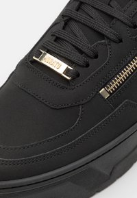 Baskets noires avec des lacets noirs épais, fermeture éclair dorée sur le côté et étiquette métallique dorée sur les lacets gravée de "MORATO."