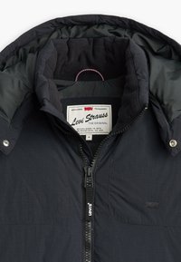 Black puffer jacket with a zippered front, fleece-lined collar, and logo tag. Features a smooth outer shell and textured inner lining.