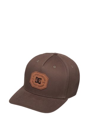 Bruine baseballpet met een gebogen klep, met een gestikte zeskantige leren patch met het "DC Shoe Company"-logo en tekst aan de voorkant.