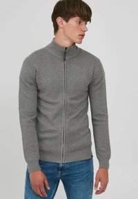 Grå zip-up sweater med et struktureret chevronmønster, ribbet krave og manchetter samt en slim fit. Båret over denim jeans.