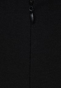 Schwarzes, mit einem Reißverschluss versehenes Kleidungsstück aus glattem, strukturiertem Stoff. Verfügt über einen mittig angebrachten Zipper und eine Naht auf der Rückseite. Geeignet zum Schichten.