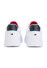 Λευκά αθλητικά παπούτσια με λείο συνθετικό επάνω μέρος, κόκκινη επένδυση, ναυτικό μπλε λεπτομέρεια στη φτέρνα και ένα μικρό λογότυπο στο πίσω μέρος. Επίπεδη σόλα από καουτσούκ.