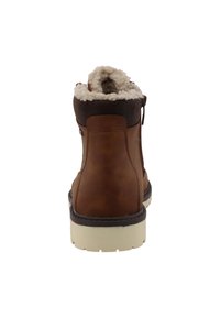 Cizmă de gleznă din piele maro cu căptușeală din blană, vârf rotund și talpă din cauciuc alb. Are un fermoar lateral și un șnur superior de culoare maro închis.