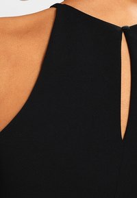 Vestido negro sin mangas con un corte tipo ojal en la espalda, fabricado con una tela suave y con un cierre de botón en el escote.
