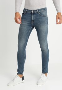 Slim blårandiga jeans med blekta detaljer, design med fem fickor och stängning med knapp. Kombinerade med vita sneakers för kontrast.