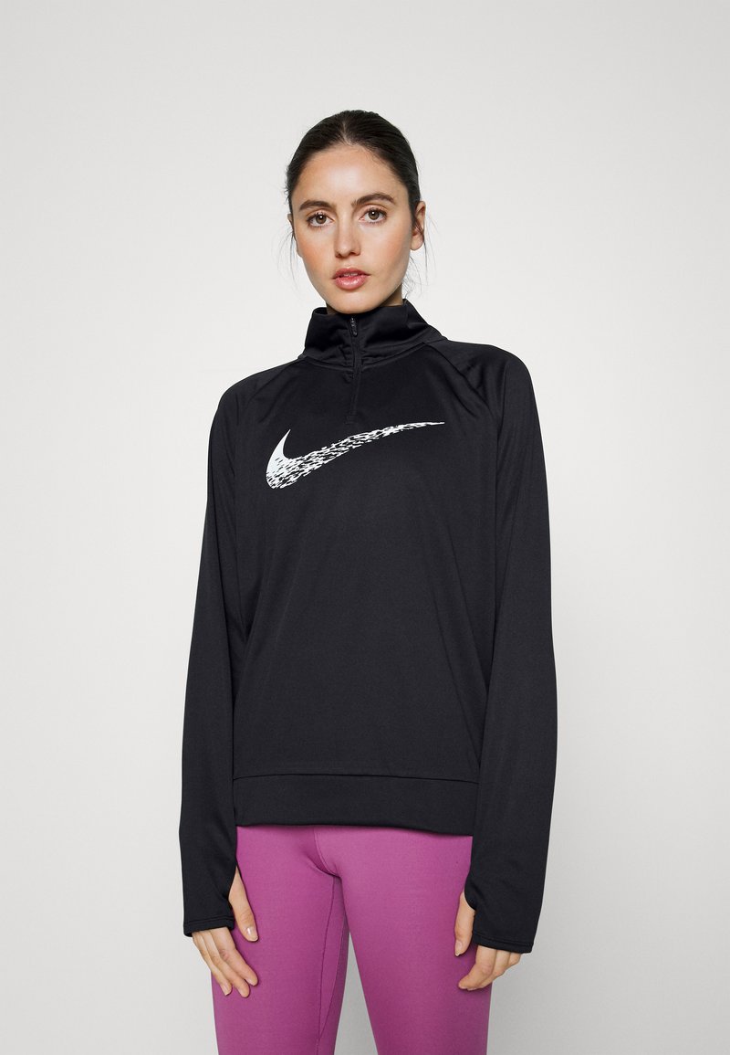 Top sportivo nero a maniche lunghe con zip a quarto, con il logo Nike bianco sul petto. Indossato con leggings viola. Tessuto liscio e elasticizzato.