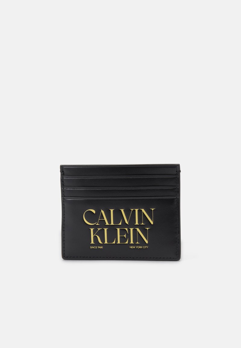 Černý kožený držák na karty má šest slotů, zlatě embosované logo "CALVIN KLEIN" a další text "SINCE 1968 NEW YORK CITY" na dně.