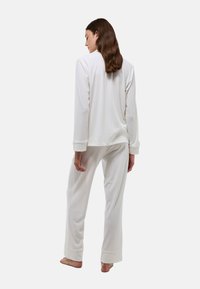 Pyjama blanc en tissu texturé, avec des manches longues et un pantalon décontracté à poignets retroussés, vu de dos.