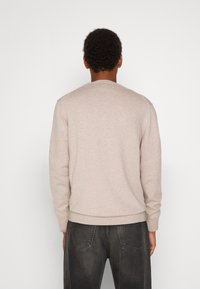 Beżowy sweter dzianinowy z okrągłym dekoltem, prążkowanymi mankietami i dołem, zestawiony z ciemnoszarymi dżinsami. Gładka faktura i swobodny krój.