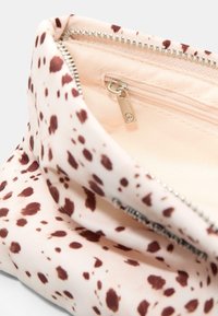 Weiche rosa Stofftasche mit unregelmäßigen dunklen braunen Flecken, teilweise geöffneter Metallreißverschluss, der ein inneres kleines Reißverschlussfach mit silbernem Zugtab offenbart.