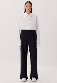 Geknipte witte overhemd met lange mouwen, gecombineerd met hoogwaist, wijde, marineblauwe broek en witte sneakers. Soepele texturen, minimalistisch ontwerp.