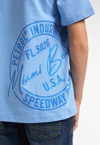 Camiseta de algodón azul claro con un gran gráfico circular azul que presenta el texto "PETROL INDUSTRIES", "Miami Beach" y "U.S.A.".
