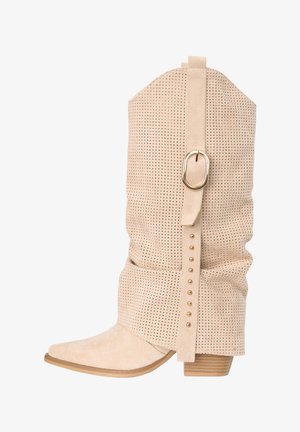 Stivale beige in camoscio a metà polpaccio con design traforato, cinturino decorativo con fibbia dorata e borchie, punta appuntita e tacco basso a blocco.