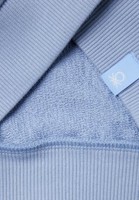 Primer plano de tela acanalada azul claro doblada para revelar el interior suave y texturizado de felpa y una pequeña etiqueta de tela azul con logotipo blanco.