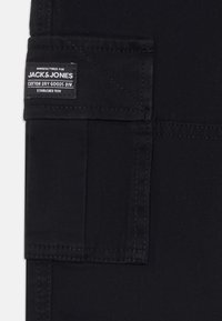 Fekete anyagú cargo nadrág oldalsó zsebbel, varrott részletekkel és "JACK & JONES COTTON DRY GOODS DIV." felirattal ellátott címkével.