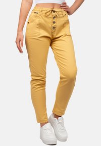 Pantalons jaune taille haute avec cordon de serrage, fermeture à cinq boutons à l'avant, deux poches et coupe slim. Associés à des baskets blanches.