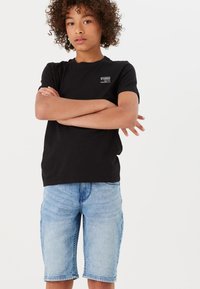 T-shirt nera con piccolo logo sul petto, abbinata a pantaloni corti in denim azzurro chiaro con taglio dritto e orli rifiniti.