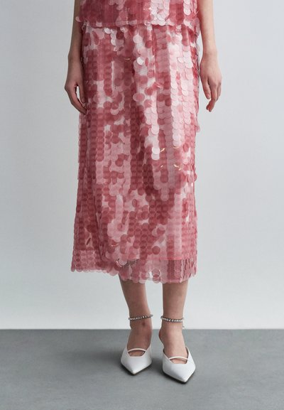 Pink sequined skirt with a layered design, featuring round reflective sequins. Worn with white pointed shoes and an ankle accessory.