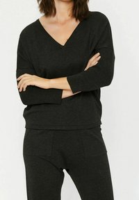 Mustapaita, jossa on pitkät hihat, V-kaula-aukko ja ribbikuvio. Yhdistetty samansävyisiin mustiin alaosiin, joissa on sivutaskut.