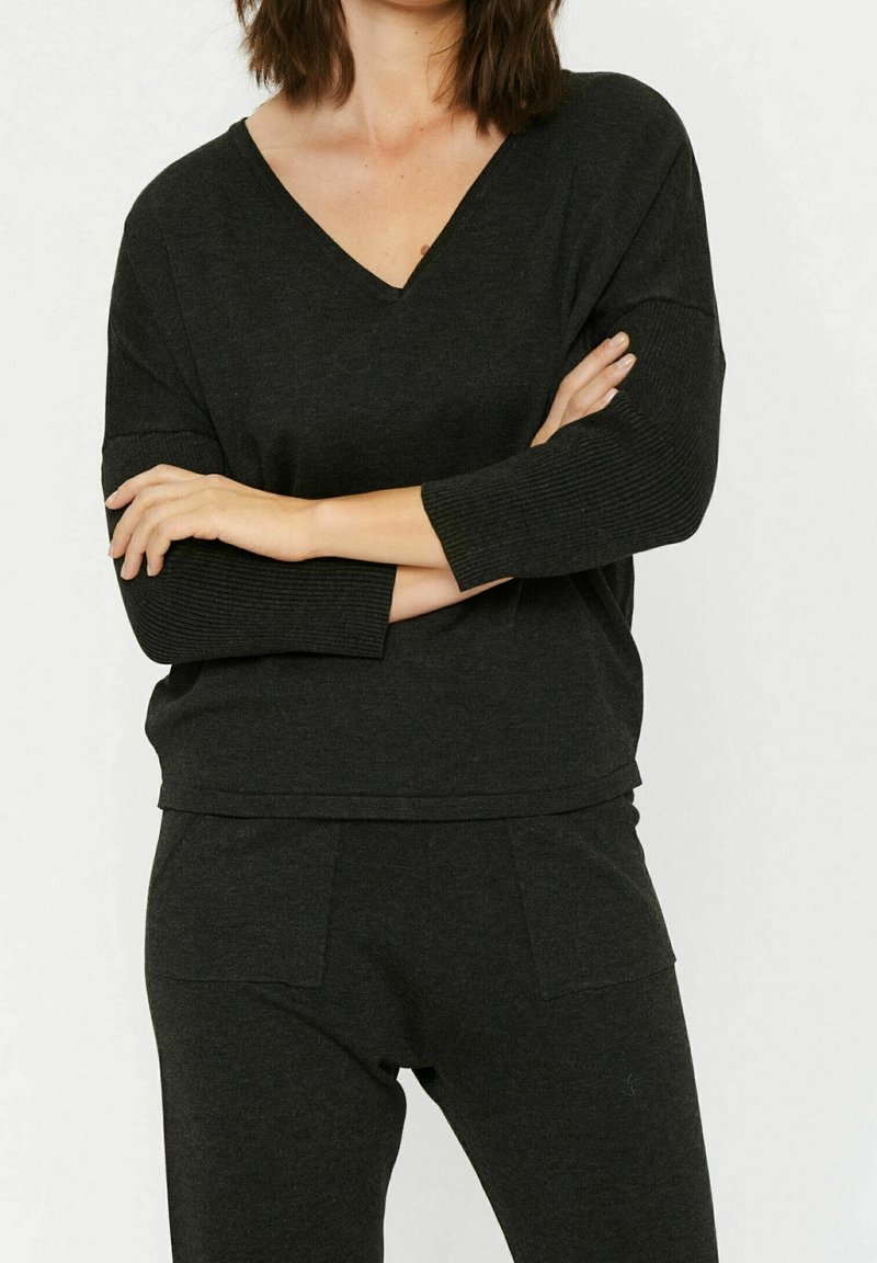 Mustapaita, jossa on pitkät hihat, V-kaula-aukko ja ribbikuvio. Yhdistetty samansävyisiin mustiin alaosiin, joissa on sivutaskut.