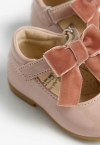 Chaussures en cuir verni rose avec un nœud en velours, fermeture à bride et finition lisse. L'intérieur est doublé et présente une semelle intérieure rembourrée.