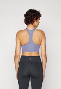 Lys lilla sports-bh i stoff med racerback-design. Båret med sorte leggings som har et logo på livet.