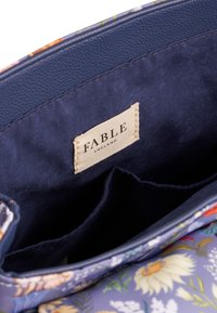 Intérieur de sac à main à motif floral ; doublure en tissu marine avec une étiquette indiquant "FABLE ENGLAND". Comprend deux poches et un matériau bleu texturé.