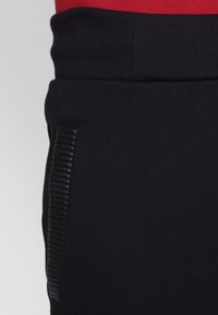 Czarne spodnie dresowe z prążkowanym pasem i teksturowanym detalem na bocznej kieszeni. Materiał wydaje się miękki i gładki.