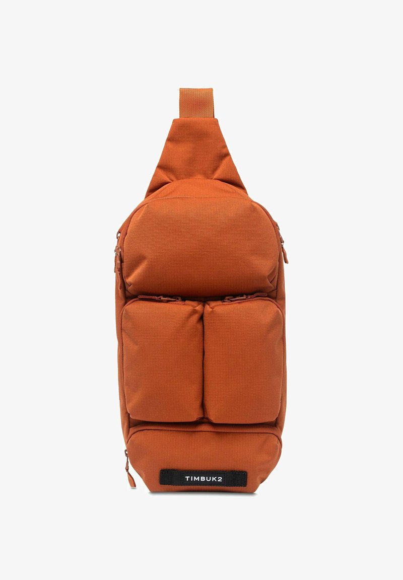 Oranje stoffen schoudertas met een bovenste strap, voorzien van drie voorste ritszakken, een strak ontwerp en een zwart TIMBUK2-label.