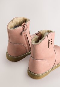 Bottines en cuir rose avec doublure en fausse fourrure, fermeture éclair et semelle en caoutchouc texturée. Présentent des détails cousus et un talon renforcé.