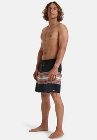 Bañador negro con patrón de rayas horizontales en beige, rojo y azul. Cintura elástica con cordón. Sin logotipos visibles.