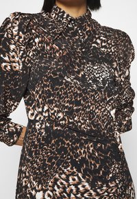 Leopardmönstrad blus med svart bas, som har nyanser av brunt och kräm. Designad med krage och puffärmar.