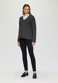 Szary sweter z dzianiny z dekoltem w serek, długimi rękawami i ribbowymi mankietami. W połączeniu z czarnymi leggingsami we wzory i błyszczącymi czarnymi loafersami.