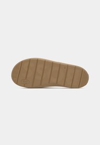 Semelle de chaussure en caoutchouc de couleur beige avec une surface texturée, présentant de profondes rainures horizontales et un marquage subtil pour l'adhérence et la durabilité.