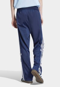 Pantalones de chándal deportivos en navy, fabricados con tela suave, que presentan franjas laterales blancas, botones a presión y una cinturilla elástica para mayor comodidad.